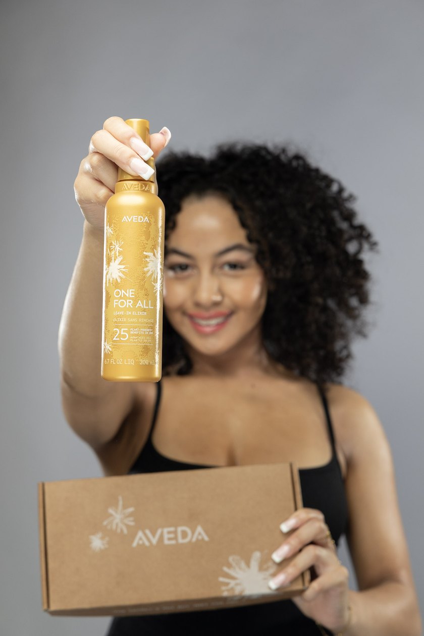 A stylist at Amenities holding the Aveda One For All Leave-In Elixir
